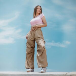 Woman posing outdoors in casual clothing against a bright sky, showcasing modern fashion trends.