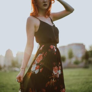 A woman with red hair poses in a stylish floral skirt outdoors during sunset in Baku.